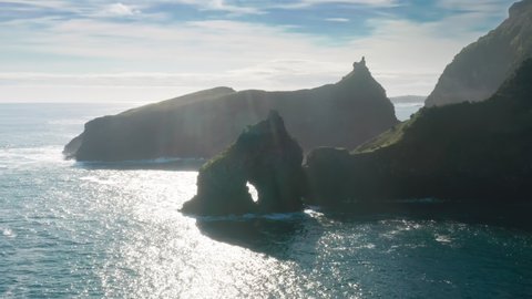 Panoramic view of ocean waves washing rocky island of Flores at sunny day, Casa do Gato Tomas, Azores, Portugal, Europe. Drone shot of seascape with green mountains, 4k footage 