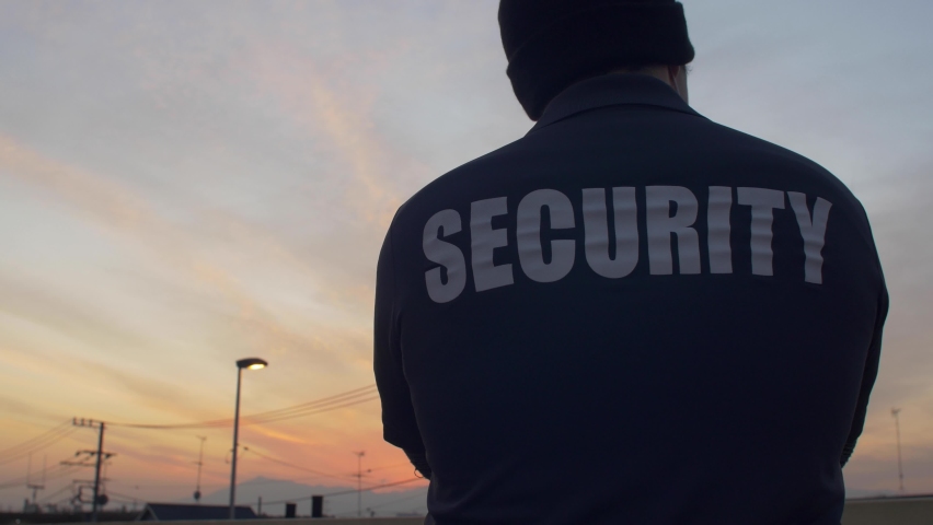 A rear view of a security guard looking down and patrolling the street and sunset. Royalty-Free Stock Footage #1072208756