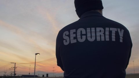 A rear view of a security guard looking down and patrolling the street and sunset.