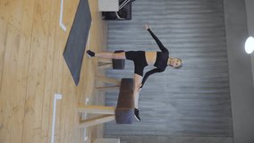 Vertical video sporty young woman exercising on gymnastic bars in fitness gym. Stretching exercises, regular sport, dressed in a black top and leggings