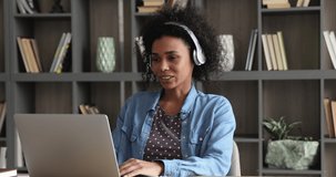 Attractive African business woman wear headphones participate at video conference with colleague by video call app on laptop. Remote study or negotiations, usage of internet and modern tech concept