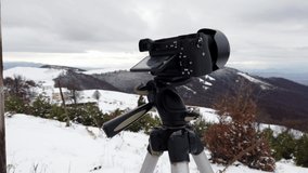 Camera on a tripod recording a time lapse of the snowy mountain peak with dark rainy clouds