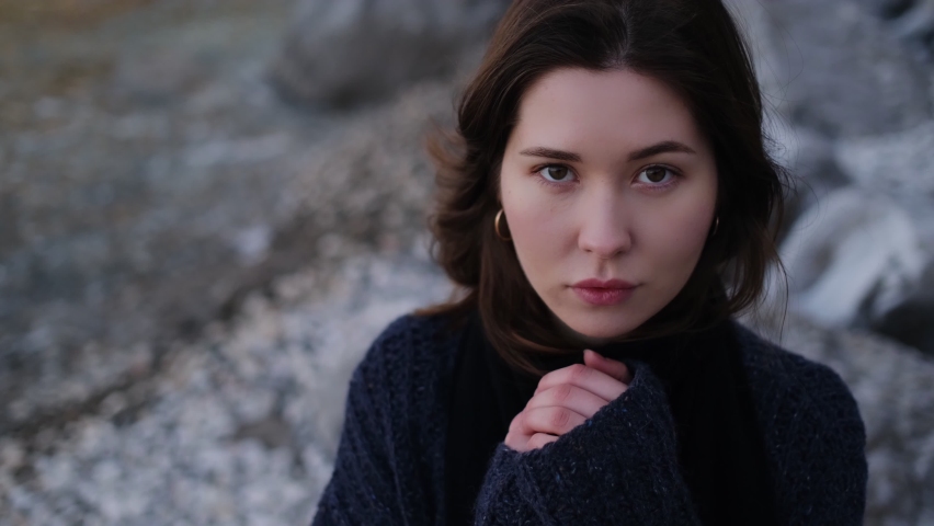 A beautiful young Asian woman in black coat on the seashore with rocks, Brunette female enjoying Loneliness by the sea.