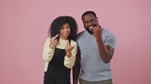 Stay back. Young african american man and woman looking at camera and showing fuck off gesture, demonstrating middle finger, purple studio background