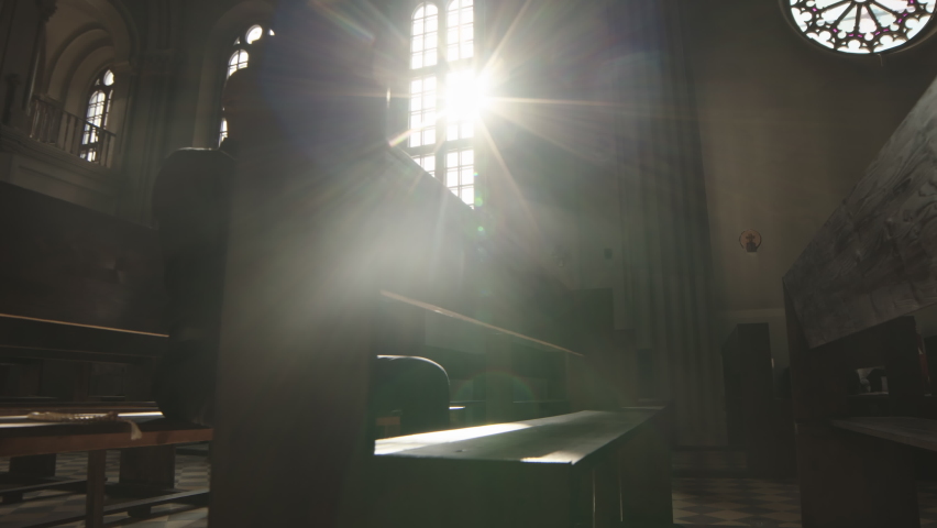 Tracking left of African-American pastor wearing black shirt and white collar sitting on wooden bench in Catholic church with Bible in hands and praying Royalty-Free Stock Footage #1072224035
