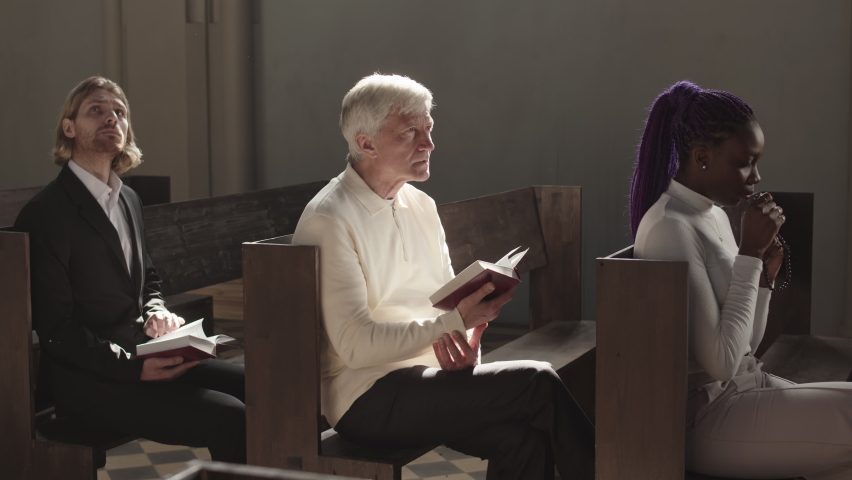 Lockdown of two diverse men and woman of different age sitting on pews in Christian church and praying heartily | Shutterstock HD Video #1072227689