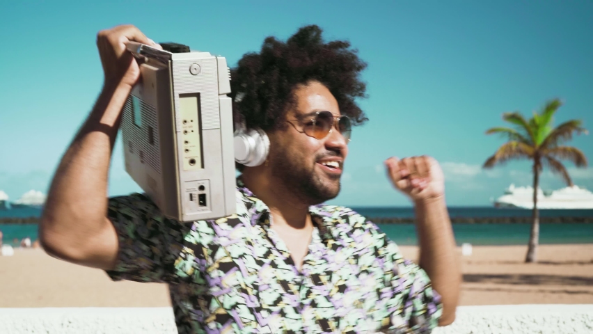 Happy Afro man having fun listening to music with wireless headphones and vintage boombox on the beach during summer time  Royalty-Free Stock Footage #1072227983
