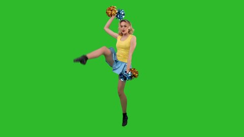 A cheerleader is dancing a jubilant dance, spinning, gracefully squatting, doing a vertical split. A blonde in a yellow and blue uniform is training in the studio on a green screen. Slow motion.