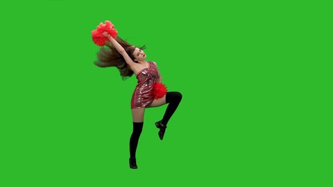 Slim cheerleader with long hair dances with red pompoms. The girl performs a jubilant dance in the studio on a green screen. Slow motion.