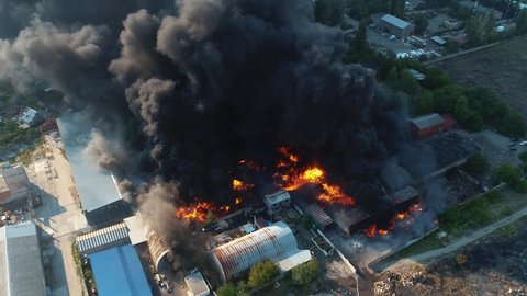 Severe fire in the warehouse. Black smoke in the sky. Drone filming over a large-scale fire. Video with grain
