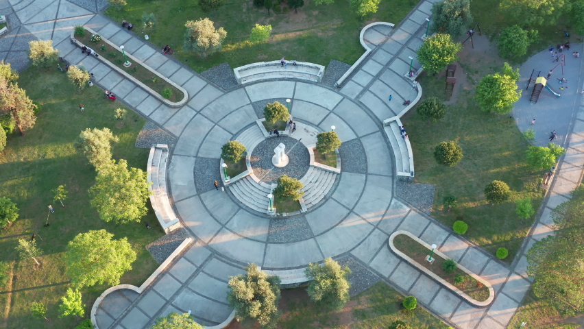 Park - round paved playground in a garden surrounded by trees and grass, as the central square of green city recreational area in urban environment. Aerial drone view of walkways and podium.