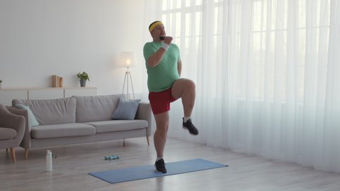 Sports beginner. Funny mature man wearing sport clothes practicing active cardio workout at home, running in place, trying to lose weight before summer, slow motion