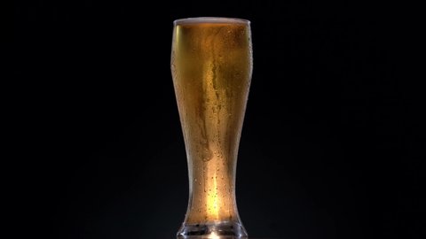 Glass of black beer on a black background. Beer sways in the glass, bubbles and foam rise