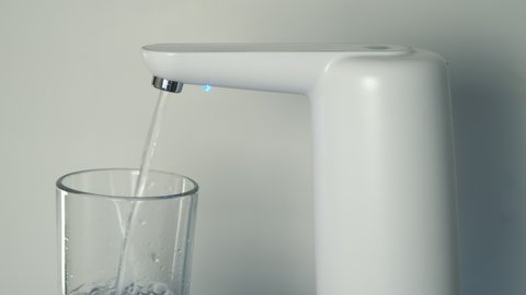 Clear water is pouring into glass from an automatic water cooler, closeup view. Pouring fresh clear water from filter to glass. Clean drinking bottled water from the well.