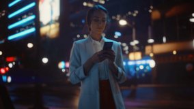 Beautiful Woman Standing, Using Smartphone on a City Street with Neon Bokeh Lights Shining at Night. Smiling Beautiful Female using Mobile Phone. Medium to Close-up Dolly Cinematic Flare Shot