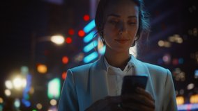 Beautiful Woman Standing, Using Smartphone on a City Street with Neon Bokeh Lights Shining at Night. Smiling Beautiful Female using Mobile Phone. Medium to Close-up Dolly Cinematic Flare Shot - Powered by Shutterstock - Get 15% off with code: PIKWIZARD15