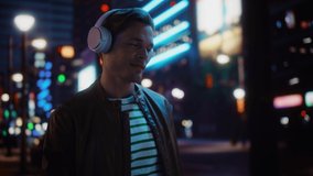 Portrait of Handsome Man Wearing Headphones Walking Through Night City Street Full of Neon Light. Smiling Stylish Man Listening to Music, Enjoying Podcast, Talk Show. Dolly Tracking Medium Shot - Powered by Shutterstock - Get 15% off with code: PIKWIZARD15