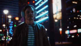 Portrait of Handsome Man Wearing Headphones Walking Through Night City Street Full of Neon Light. Smiling Stylish Man Listening to Music, Podcast, Talk Show. Dolly Tracking Medium Shot - Powered by Shutterstock - Get 15% off with code: PIKWIZARD15