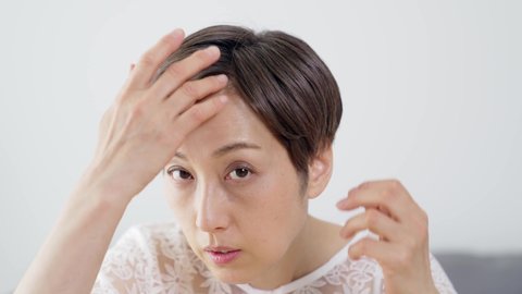 Middle aged Asian woman worrying about her hair. Beauty concept. Thinning hair. Hair care.