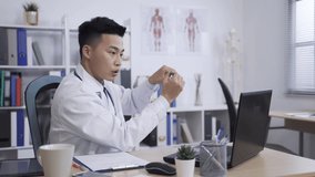 asian male doctor is gesturing with a pen in hand while sharing information during an distant consultation with his patients on the computer in clinic office.