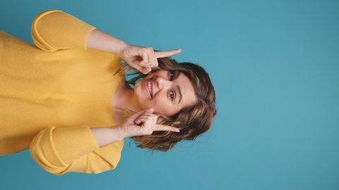 Vertical video stories reels happy young woman face close up hands up on copy space for advertising moving smiling curly hair yellow clothes on blue background Positive emotion. Holiday Lifestyle