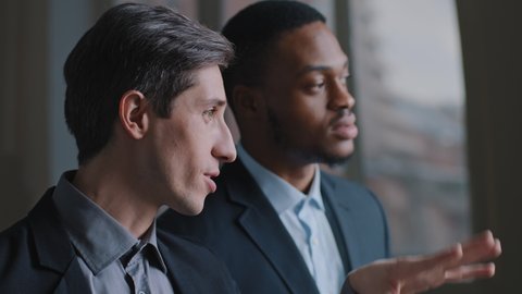 Portrait of two multiracial businessmen multinational colleagues looking out window pointing fingers discussing plan for future building, Caucasian investor and African architect talking about project