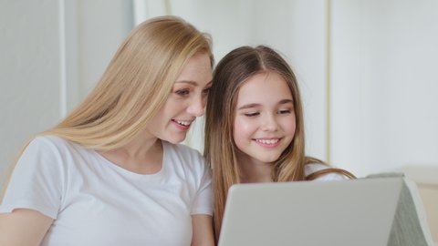 Adult beautiful mother mature woman with daughter teenage girl sitting together at home using modern laptop to watch movies funny videos on web on site browsing looking at computer screen laughing