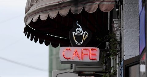 Glowing neon sign of a cafe with cup of coffee under a canopy.