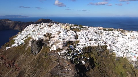 Aerial Shot Of Whitewashed City On Mountain By Sea Against Sky, Drone Flying Forward Towards White Residential Structures On Sunny Day - Santorini, Greece