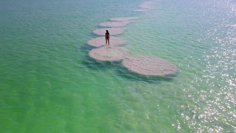 Aerial Shot Of Woman Walking On Salt Formation At Dead Sea During Vacation, Drone Flying Forward Over Lake