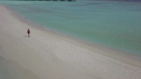 Aerial Panning Shot Of Woman Walking On Shore At Beach, Drone Flying Backward From Tourist Amidst Turquoise Sea On Sunny Day - Kuramathi, Maldives