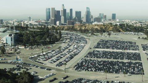 Aerial Shot Of Cars In Parking Lot At Famous Stadium, Drone Flying Backward Over Famous Landmark In City Against Sky On Sunny Day - Los Angeles, California
