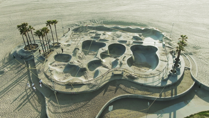 Aerial Tilt Up Shot Of People At Venice Skate Park On Sunny Day, Drone Flying Backward Over Beach Against Sky - Los Angeles, California