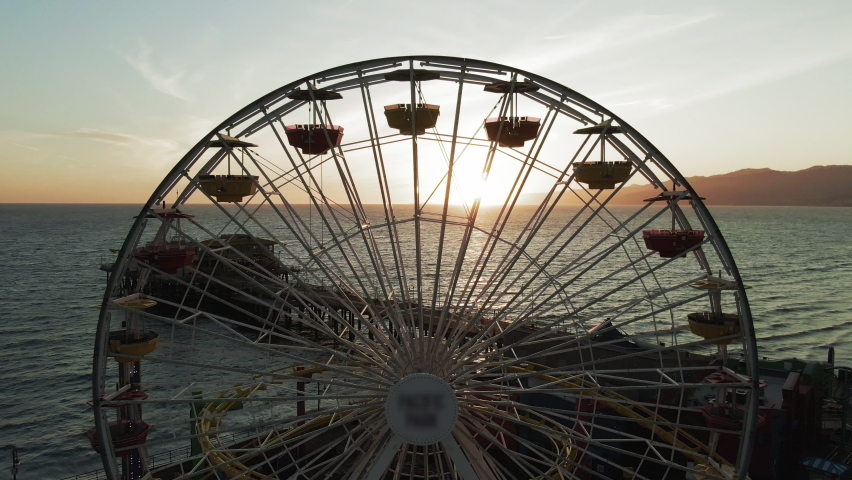 Aerial Shot Of Back Lit Ferris Wheel At Santa Monica Pier, Drone Flying Backward From Famous Landmark Over Sea Against Sky At Sunset Royalty-Free Stock Footage #1072252331