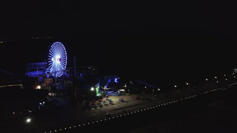Aerial Panning Shot Of Illuminated Heart Shape On Ferris Wheel At Pier, Drone Flying Over Famous Santa Monica Pier At Night