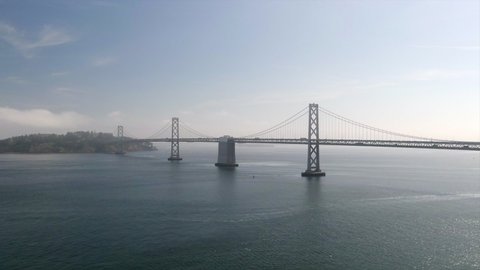 Aerial Panning Shot Of Famous Oakland Bay Bridge Over Bay Against Sky, Drone Flying Over Sea Towards Popular Landmark On Sunny Day - San Francisco, California
