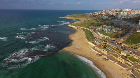 Aerial Shot Of Waves Splashing On Shore At Beach By Houses, Drone Flying Forward Over Coastal City Against Sky - Jaffa, Israel