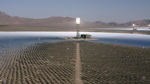 Aerial Reversing Away From A Stunning Solar Field In The Desert With Dirt, Dry Brush, Clear Blue Sky, Bright Sunlight, And Steep Mountains In The Background - Ivanpah, California