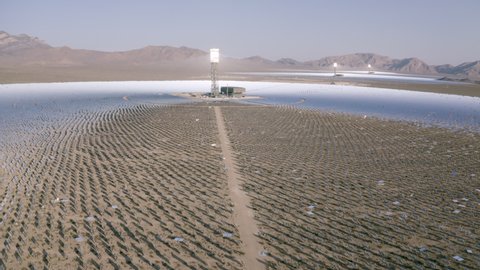 Aerial Tilt Up To Reveal A Solar Field In The Desert With Dirt, Dry Brush, Clear Blue Sky, Bright Sunlight, And Steep Mountains In The Background - Ivanpah, California