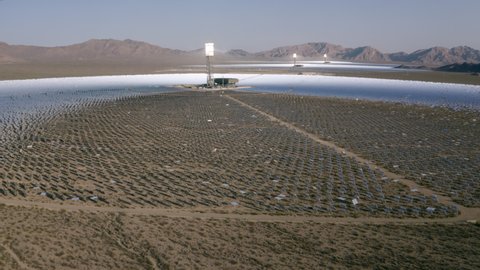 Aerial Circling A Solar Field In The Desert With Dirt, Dry Brush, Clear Blue Sky, Bright Sunlight, And Steep Mountains In The Background - Ivanpah, California