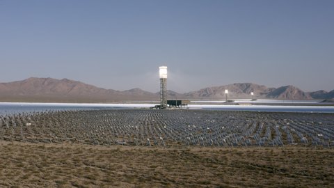Aerial Moving Forward Across The Desert To A Solar Field, With Dirt, Dry Brush, Clear Blue Sky, Bright Sunlight, And Steep Mountains In The Background - Ivanpah, California