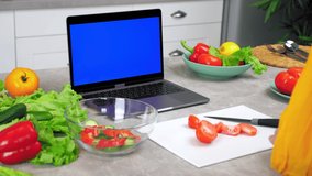 Blue screen mock up chroma key monitor laptop: Woman housewife in home kitchen slices tomato on cutting board listen tells chef shows slice tomato teacher webcam, study online video call chat computer