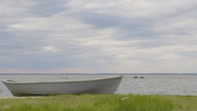 A wooden fishing boat moored on a sandy and grassy shore at sunset with a cloudy sky, time lapse.