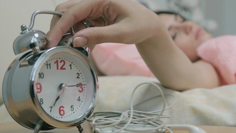 Old fashioned alarm clock rings in the morning on a table . Girl’s hand overturns the alarm so that it shuts up . Sleeping girl waking up from alarm calling and turning it off . Classic clock ringing 
