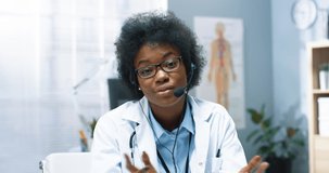 Close up portrait of cheerful African American healthcare specialist looking at camera and speaking in headset on online medical webinar, video consultation on internet, treatment concept