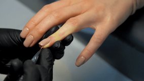 Beauty salon worker applies new layer of coloured gel on young woman nail with special brush close view. Concept trend