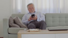 Happiness of wellness elderly asian man with white hairs sitting on sofa enjoy and using mobile phone VDO Conference online meeting with family and smile at home,Senior lifestyle at home concept