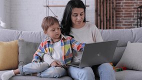Happy young mother relaxing with little kid son looking at laptop screen webcam having fun using funny face mask effects making conference video call chat at home relaxing laughing sitting on sofa.