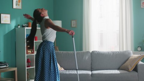 Young energetic woman has fun at home, dancing and rejoicing, imagine herself a star, then continues cleaning a floor with a mop.