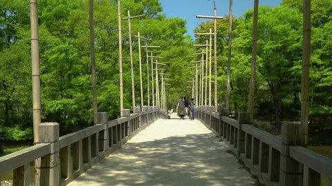 Friends Walking At An Old Wooden Bridge With Lush Green Trees At Korean Folk Village In Yongin, Seoul, South Korea. - wide static